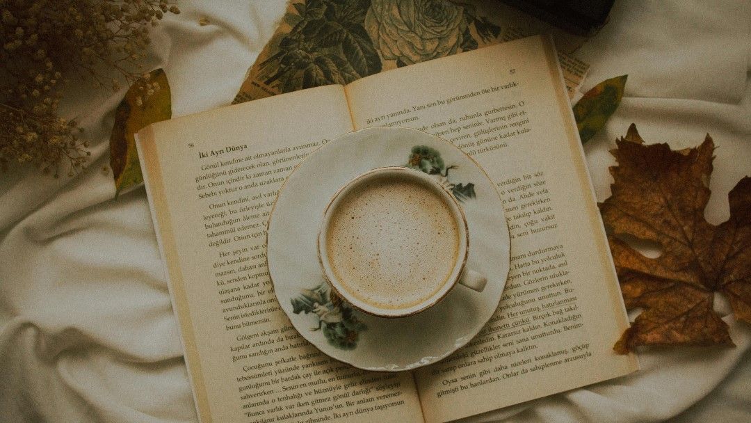 image d'une tasse de café posée sur un livre ouvert dans un décor automnal